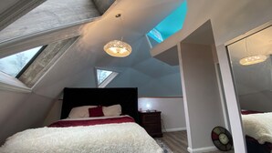 Ein Schlafzimmer mit Dachfenster, einem Bett mit weißer und roter Bettwäsche, einem Nachttisch und einer Wanduhr.