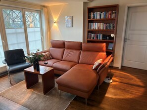 Un soggiorno con un divano in pelle marrone, una poltrona nera, un tavolino in legno e una libreria piena di libri.