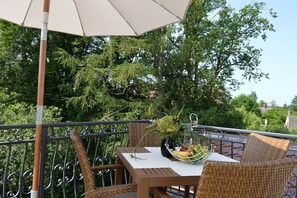 Un balcone con mobili in vimini, un tavolo con una ciotola di frutta e un ombrellone grande.