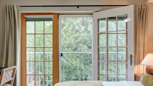 A bedroom with a large bed, a chair, a wooden desk, and a view of greenery through the sliding glass doors. - 261 S 17th Street (Philadelphia)