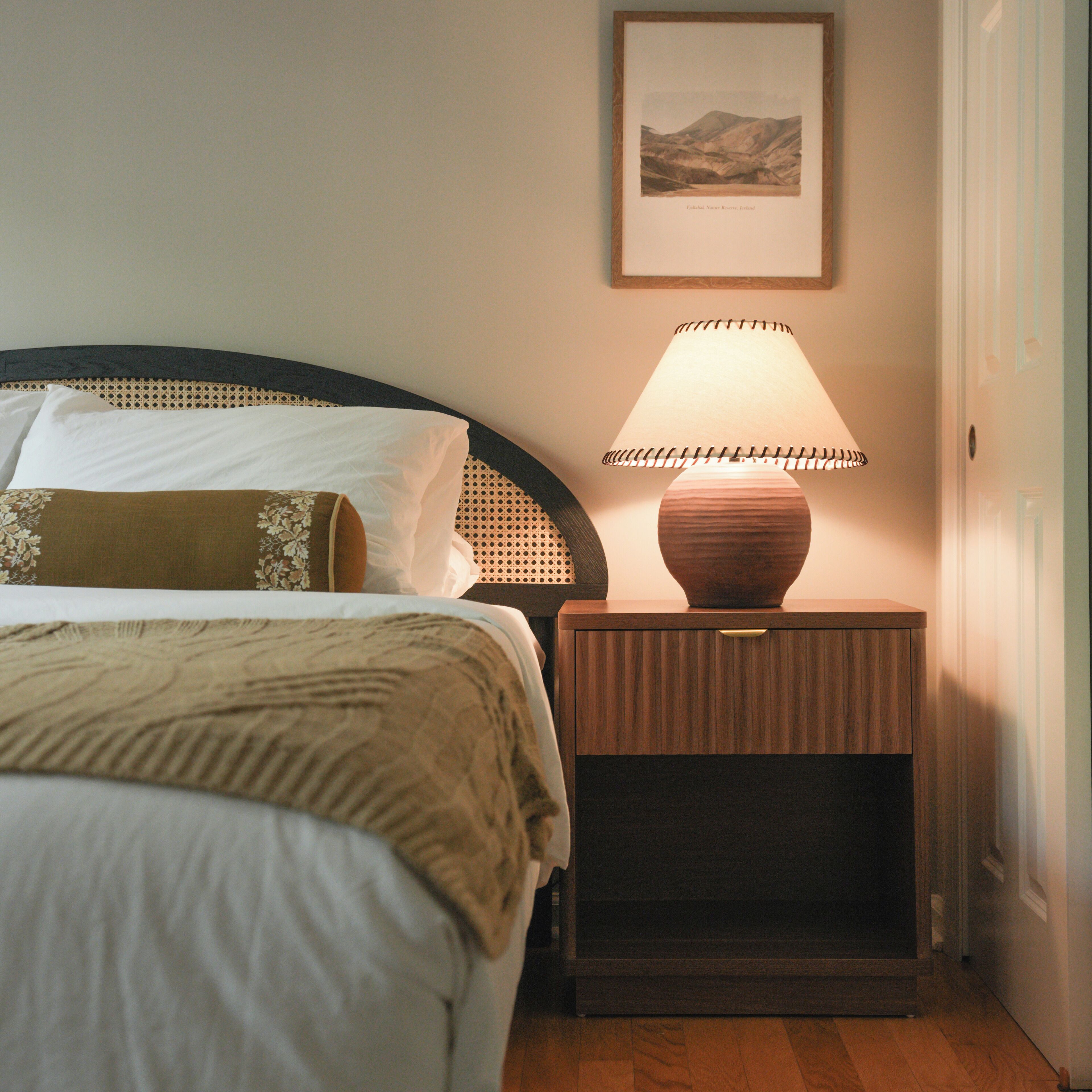 A neatly made bed with a headboard, a bedside lamp, and a framed picture on the wall.