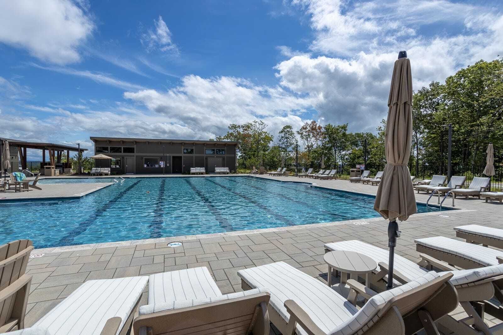 Une piscine avec des chaises longues et des parasols, un espace de repos couvert et un bâtiment en arrière-plan.