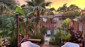 Eine Holzterrasse mit zwei weißen Stühlen, umgeben von üppigen tropischen Pflanzen und einem Holzzaun.