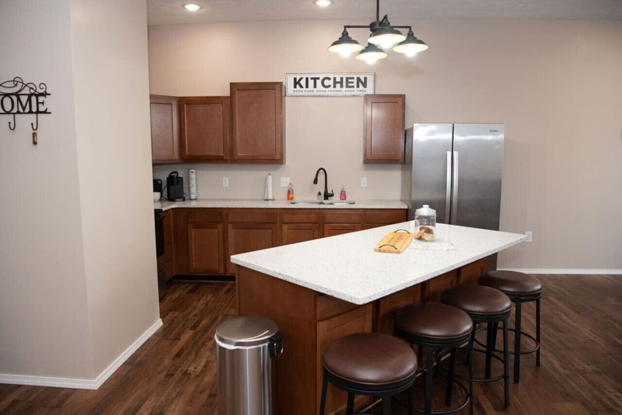 A modern kitchen with wooden cabinets, a stainless steel refrigerator, a white countertop, and a bar stool seating area.