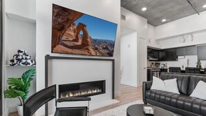 A modern living room with a fireplace, a large flat-screen TV, a leather sofa, and a kitchen area in the background. - Premium SLC Luxury- Penthouse VIEWS+ Top Amenities (Salt Lake City)