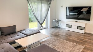 Ein modernes Wohnzimmer mit Ecksofa, Flachbildfernseher und einer schlichten, weißen Unterhaltungsecke.