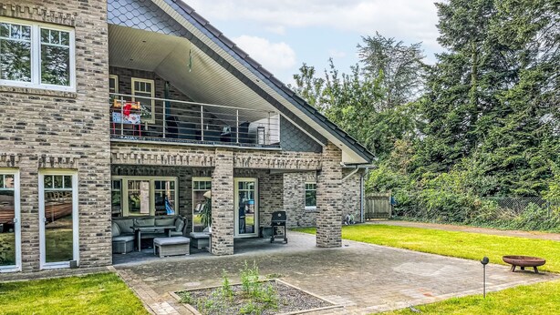 Ein zweistöckiges Steinhaus mit Balkon, Sitzgelegenheit im Freien und einem Garten.