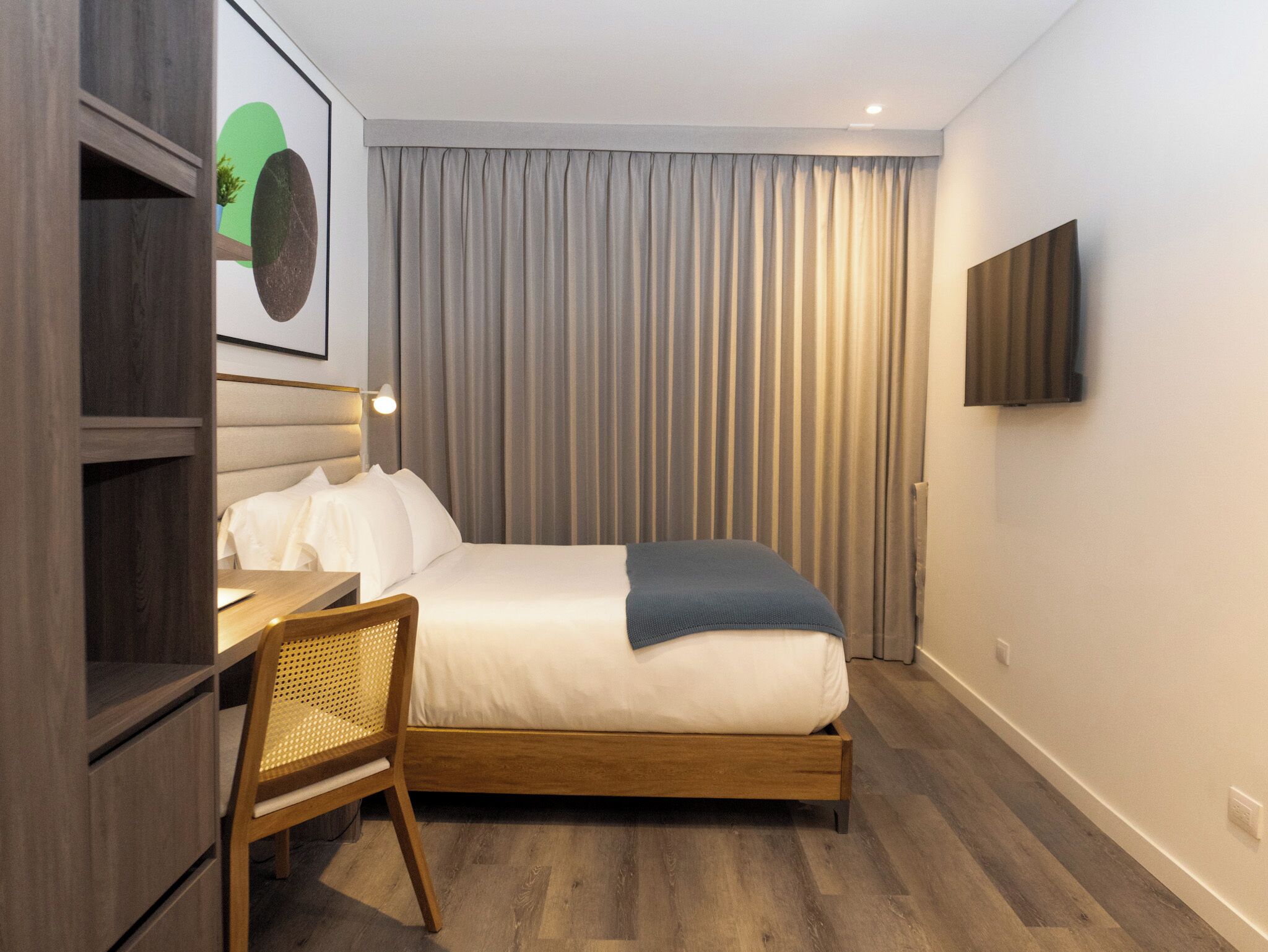 Quarto de hotel moderno com cama de madeira, uma escrivaninha e uma cadeira.