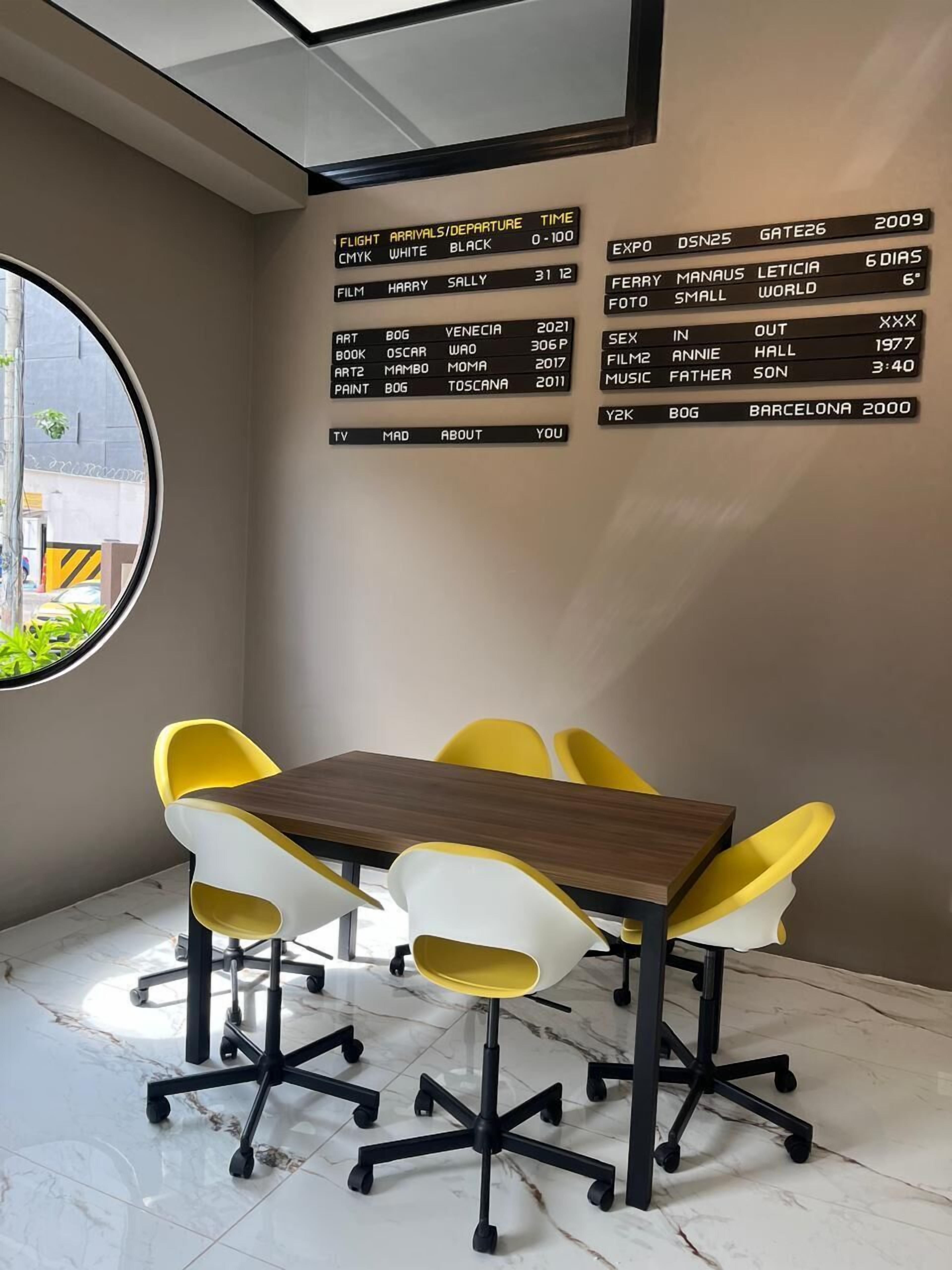 Una sala de reuniones moderna con techo de vidrio, una mesa redonda con sillas amarillas y una pizarra informativa en la pared.