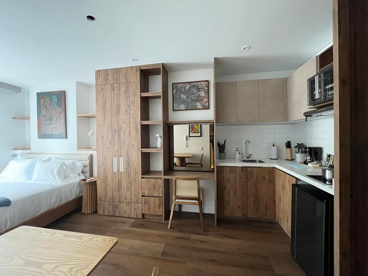 Habitación de hotel compacta con cama, escritorio y kitchenette.
