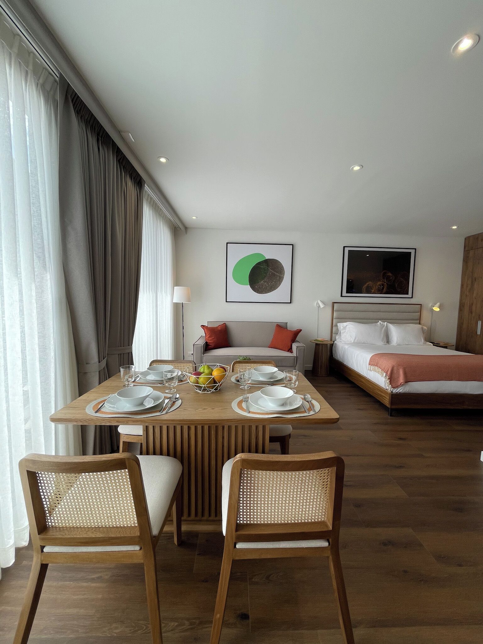 A modern hotel room with a dining area, a bed, and a large window with curtains.