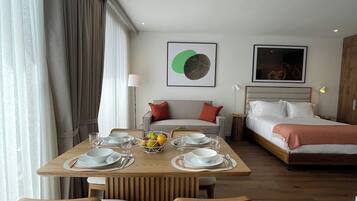 Una habitación de hotel moderna con comedor, cama y un amplio ventanal con cortinas.