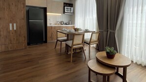 A modern kitchen with wooden cabinets, a black refrigerator, and a microwave. There is a dining area with a round table and chairs, and a potted plant on the table. - Art Homes 85 (Bogotá)