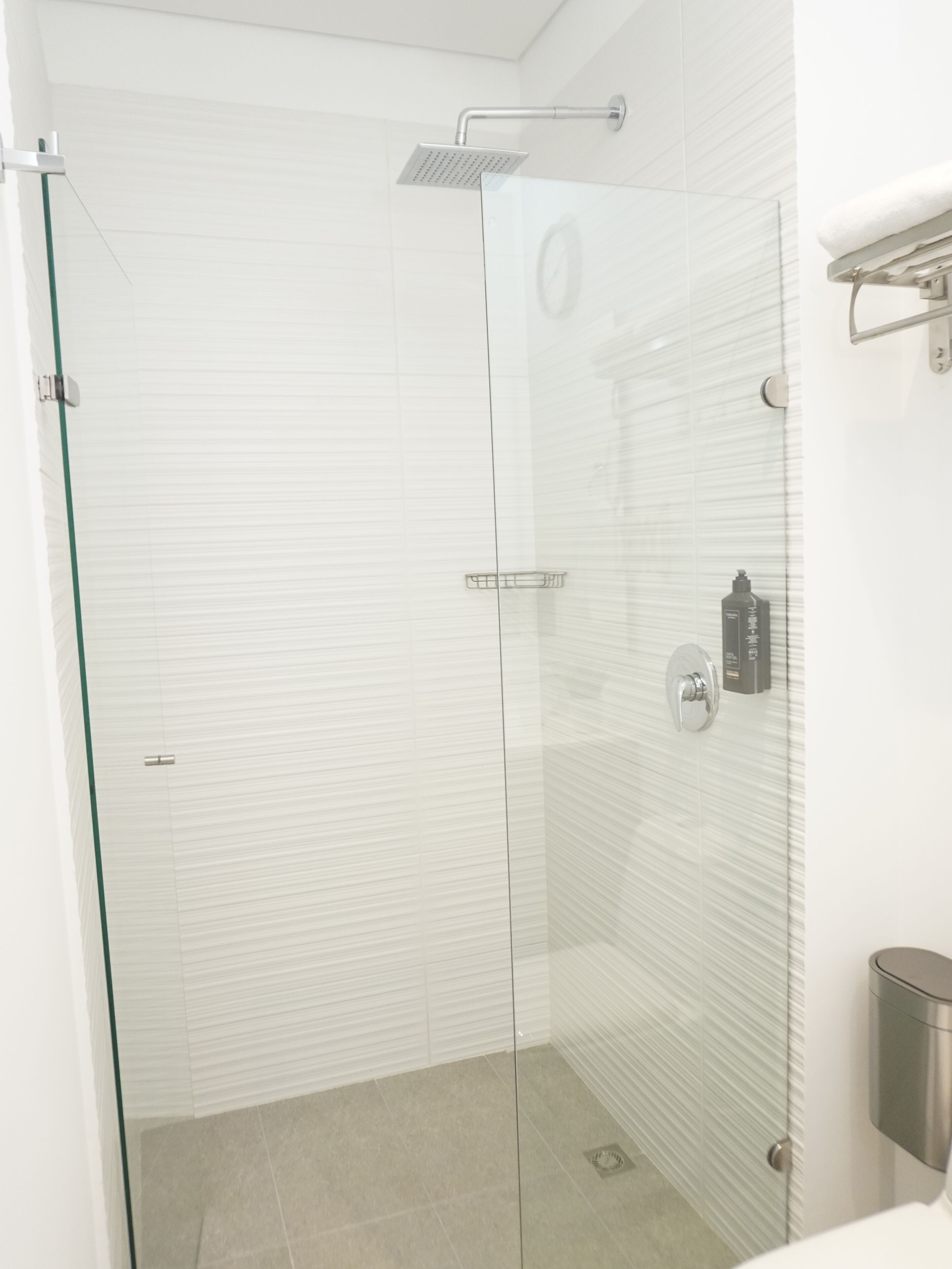 A modern bathroom with a glass shower enclosure, white tiled walls, and a stainless steel sink.