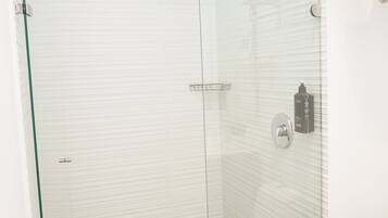 A modern bathroom with a glass shower enclosure, white tiled walls, and a stainless steel sink.