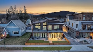 A modern multi-story residential building with a well-maintained lawn, outdoor seating area, and large windows.
