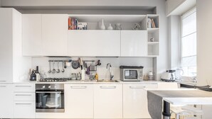 Une cuisine moderne avec des meubles blancs, un four encastré, un four à micro-ondes et une cuisinière à gaz.