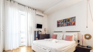 Une chambre moderne avec un grand lit, un téléviseur à écran plat, une œuvre d’art murale et une table de chevet avec une lampe.