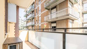 Un balcon donnant sur un immeuble à plusieurs étages, avec une rambarde en métal et une petite structure recouverte d’un treillis.