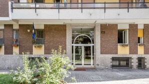 Un bâtiment à la façade en briques, doté d’une entrée en verre et d’un balcon avec des balustrades.