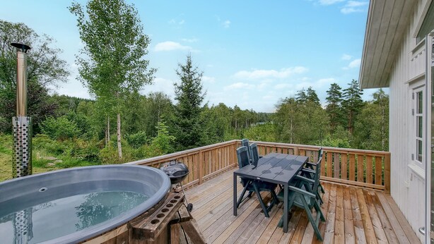 Eine Holzterrasse mit Whirlpool, Grill und Gartenmöbeln.