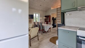 Eine Küche mit Kühlschrank, Herd und Schränken. Ein Essbereich mit Tisch und Stühlen ist ebenfalls vorhanden. Eine Leiter lehnt an der Wand.