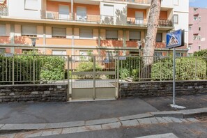 A gated residential building with balconies, a pedestrian crossing sign, and a stone wall.