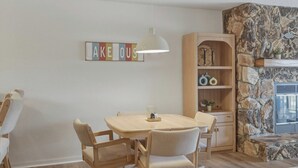 A dining area with a table and chairs, a hanging light fixture, a bookshelf, and a stone wall. - Lazy Days E-08 - Two Bedroom Apartment, Sleeps 6 (Osage Beach)