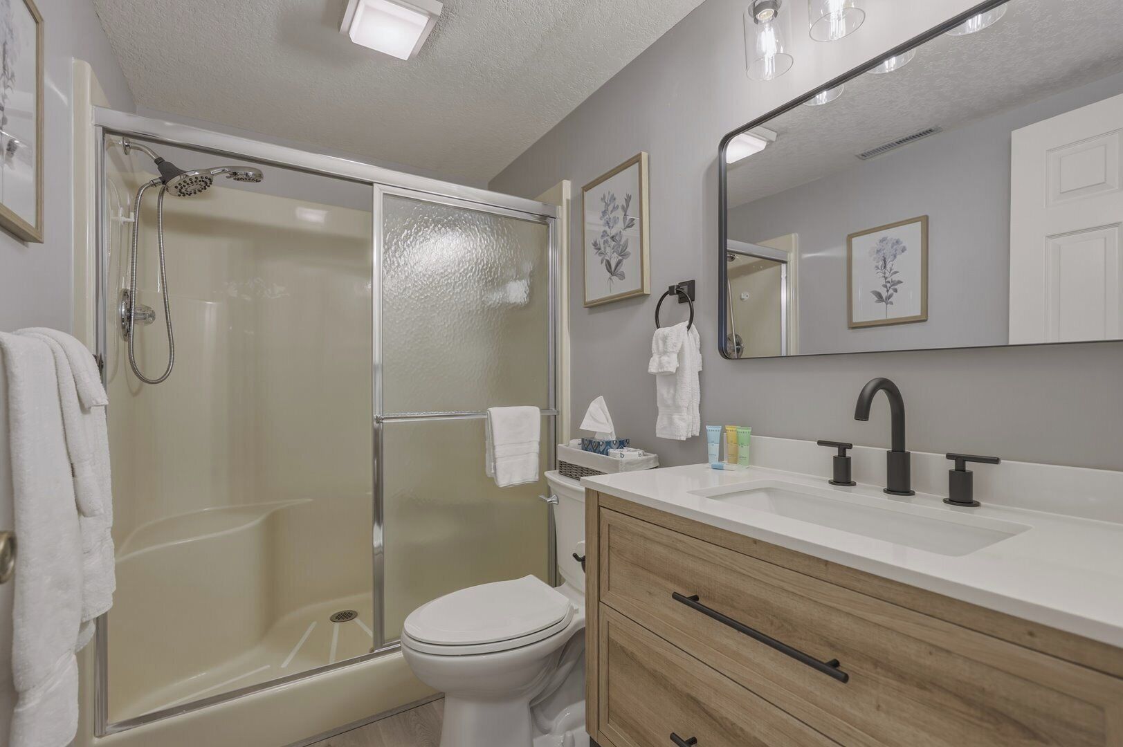 A bathroom with a glass shower enclosure, a toilet, a vanity with a mirror, and a sink.