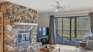 Una chimenea de piedra, un televisor, un sofá y un balcón con vistas.