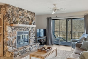 Ein Steinkamin, ein Fernseher, ein Sofa und ein Balkon mit Blick.