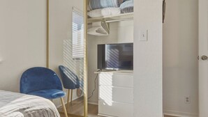 Un dormitorio con una cama, una silla azul, un armario y un televisor.