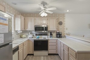 A kitchen with light wood cabinets, stainless steel appliances, a ceiling fan, and a clock on the wall.
