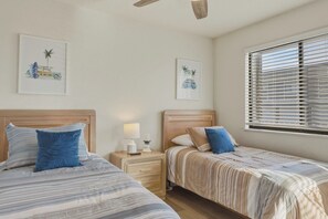 Ein Schlafzimmer mit zwei Betten, einem Nachttisch mit Lampe und Fernbedienung sowie einem Fenster mit Jalousien.