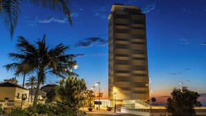 Un hotel alto y moderno con fachada a cuadros, rodeado de palmeras y un cielo despejado.