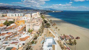 Vista aérea de una ciudad costera con playa, edificios y palmeras.