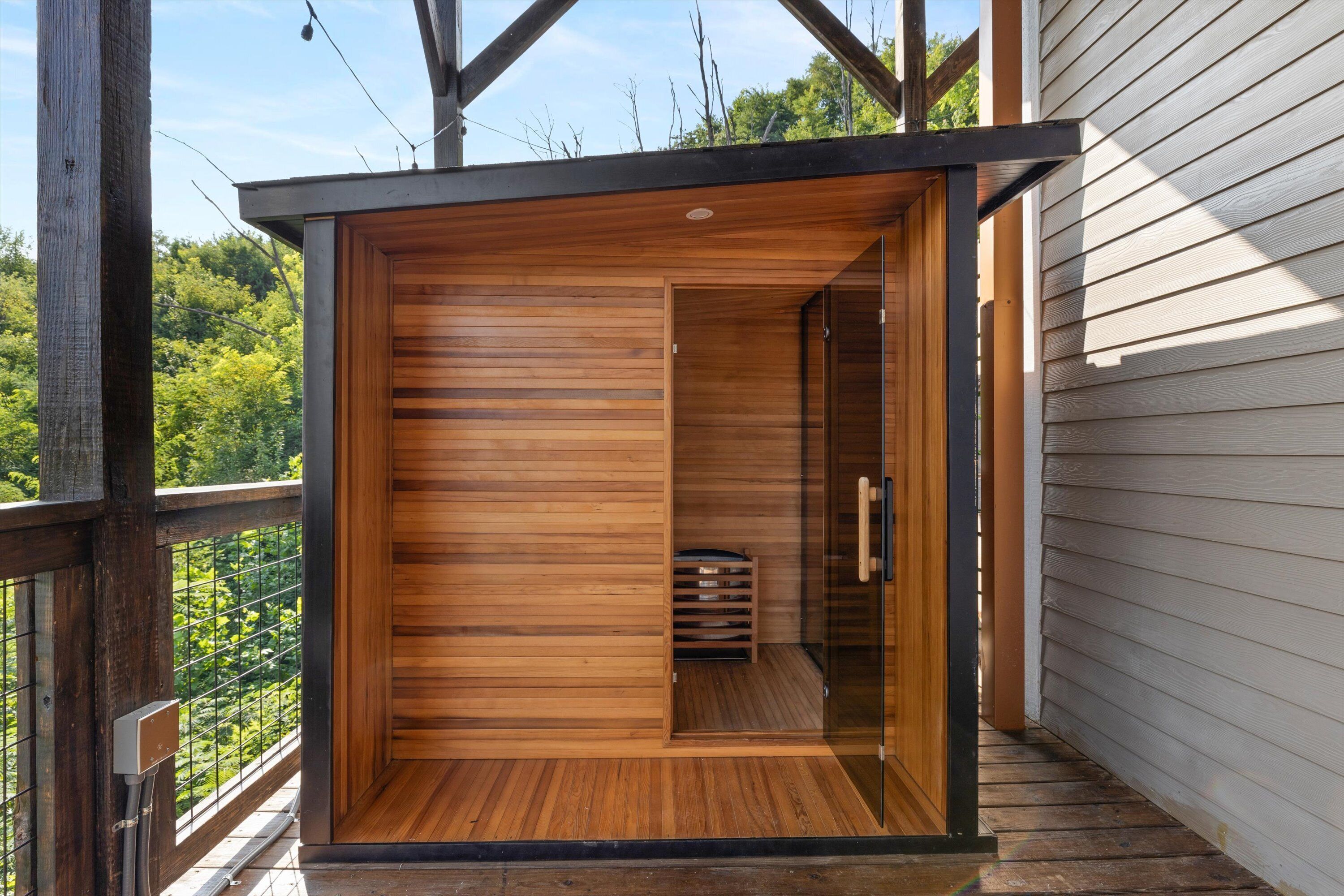 Un sauna en bois doté d’une porte en verre, d’un banc en bois à l’intérieur et offrant une vue sur la végétation environnante.