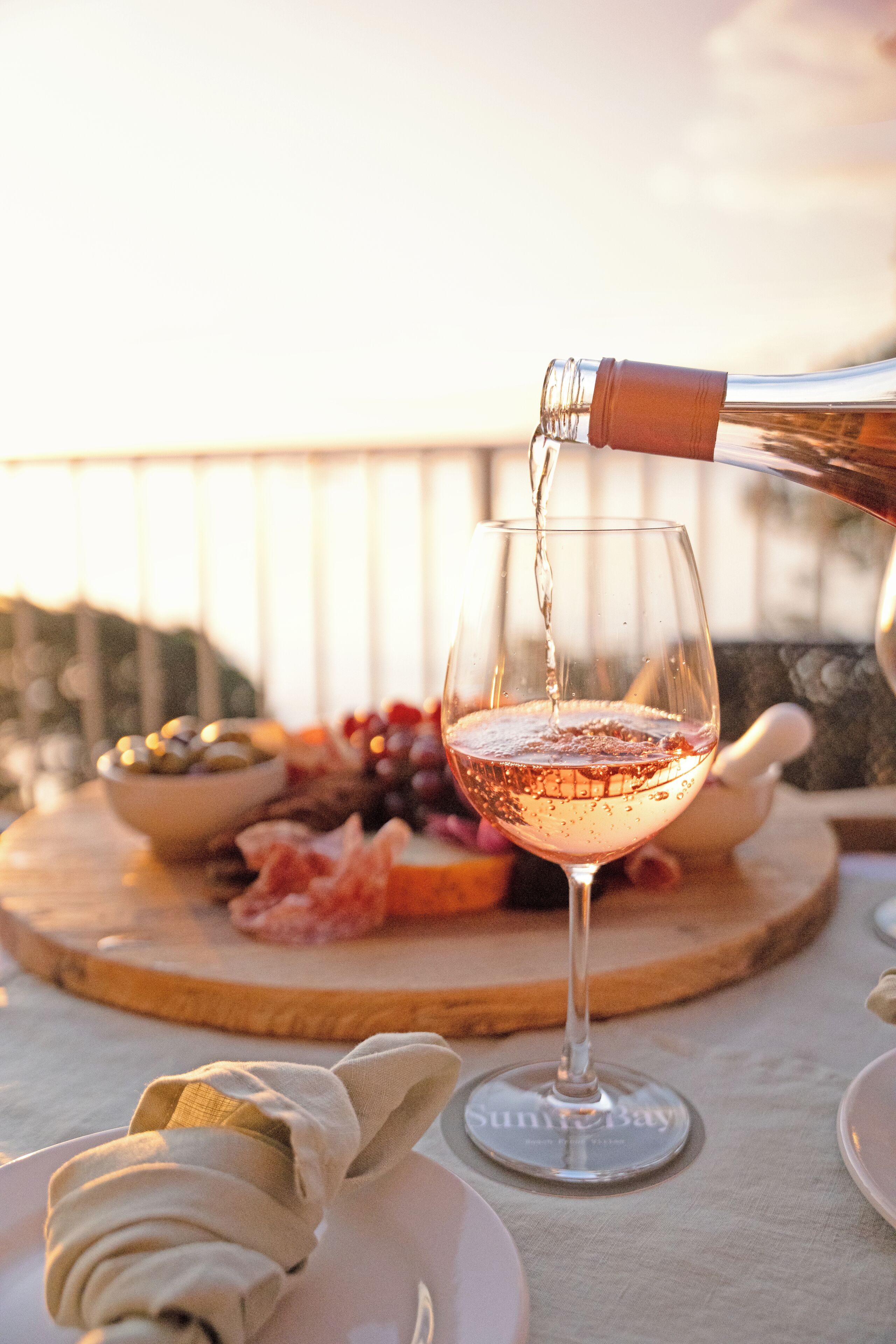 A table with a wine glass being filled, a bowl of olives, and a charcuterie board with meats and cheeses.