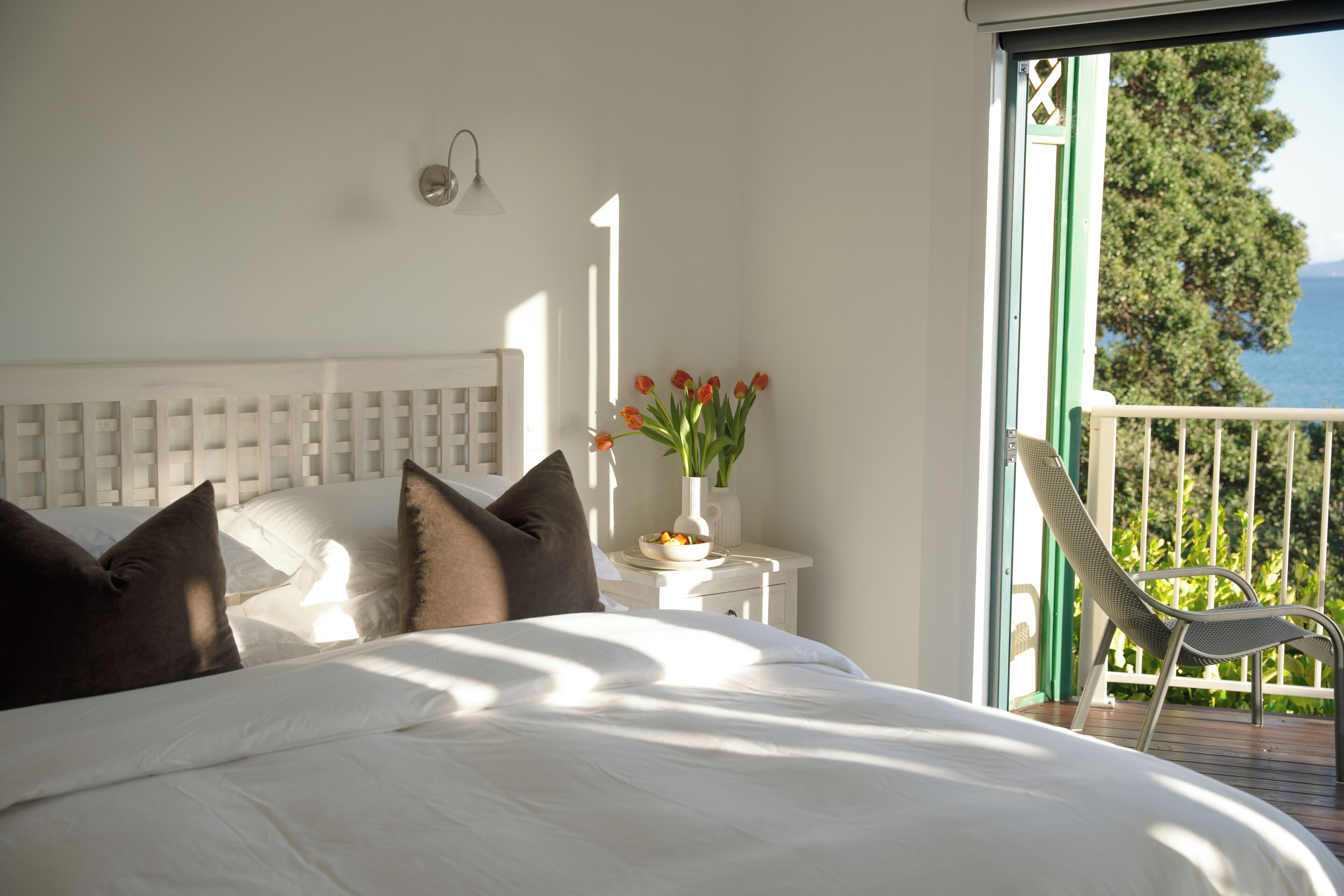Une chambre à coucher avec un grand lit, une table de chevet ornée d’un vase de fleurs et une vue sur l’extérieur.