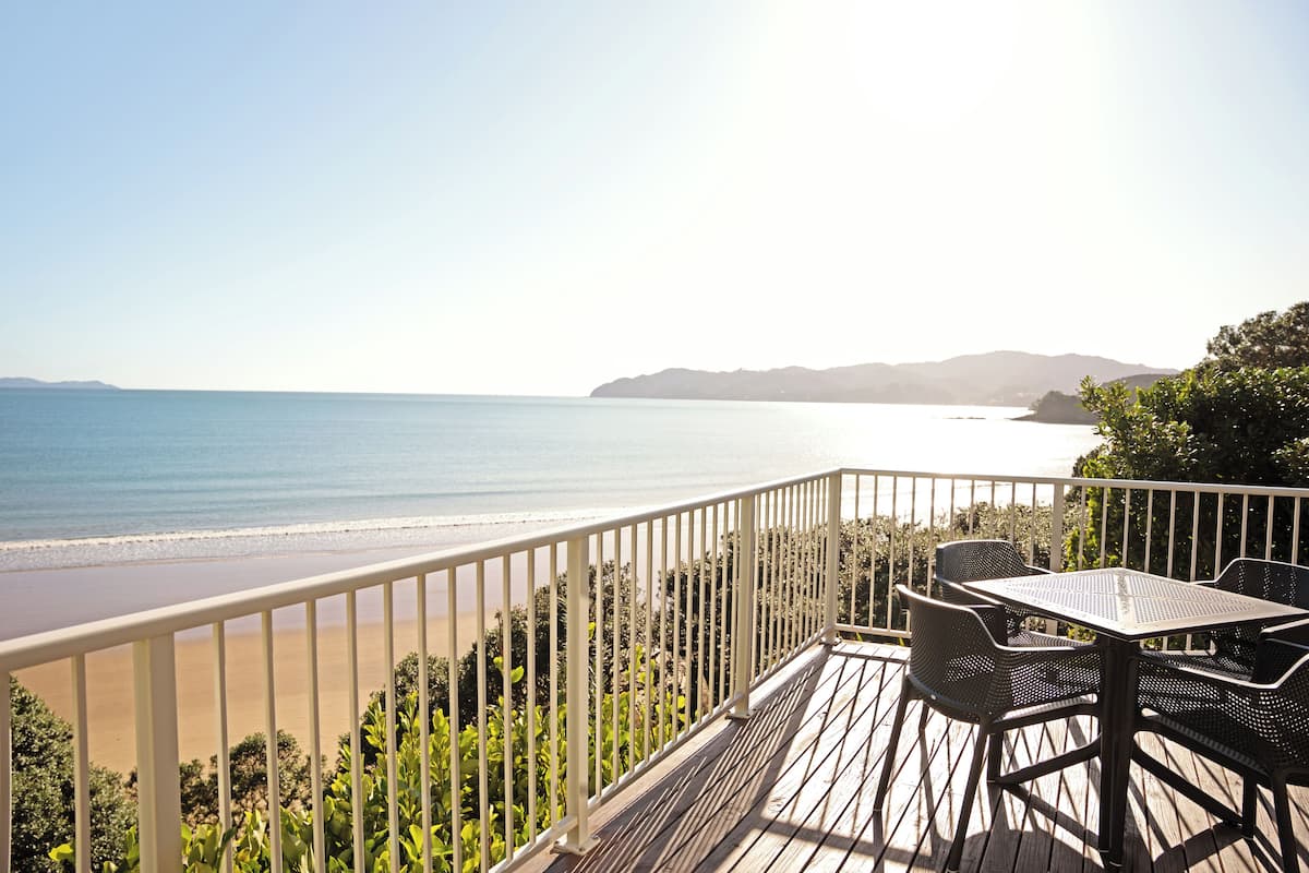 A deck with a table and chairs overlooking a beach with clear skies.