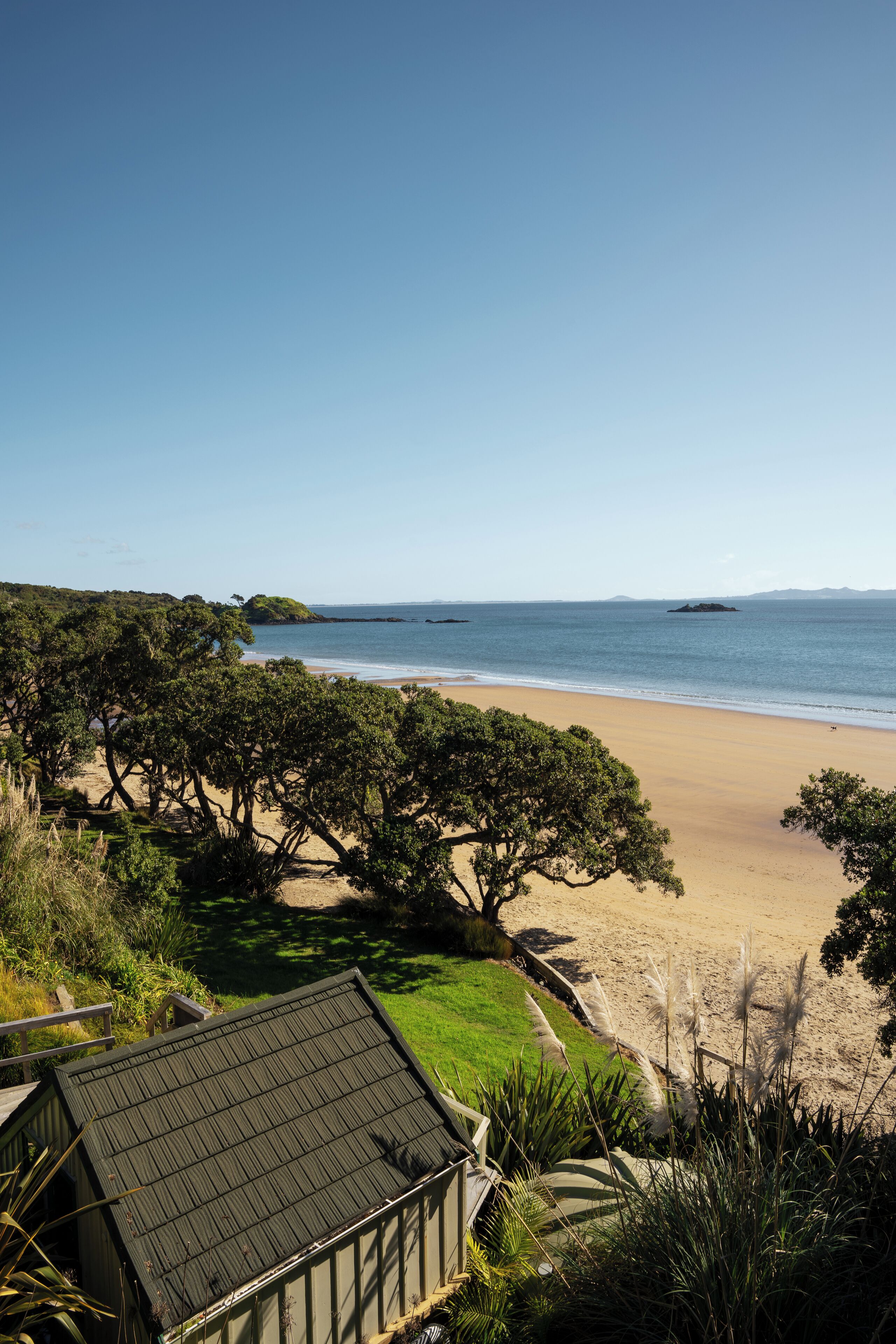 A beach view with a house and trees in the foreground.