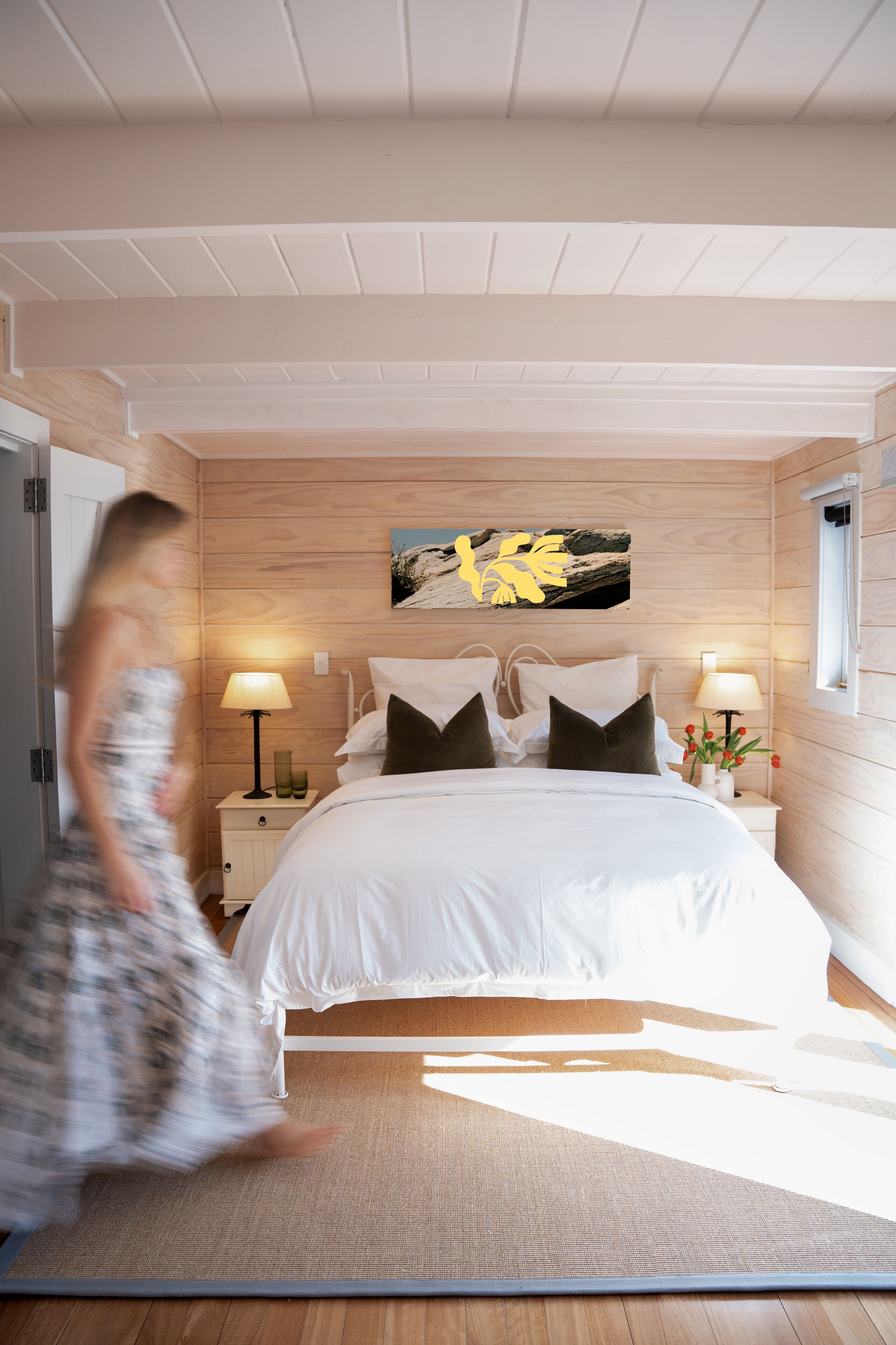 Ett sovrum med en stor säng, två sängbord med lampor, en träpanel som utgör sänggaveln och en tavla ovanför sängen.