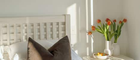 Una cama bien hecha con almohadas, una mesita de noche con un florero y una lámpara de pared.