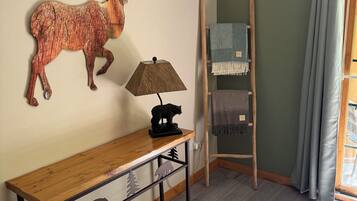 Una habitación con un banco de madera, una escultura de ciervo montada en la pared, una lámpara, una escalera y una ventana con cortinas.
