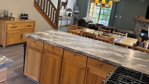 Una cocina con armarios de madera, encimeras de granito, estufa empotrada y una zona de comedor con mobiliario de madera.