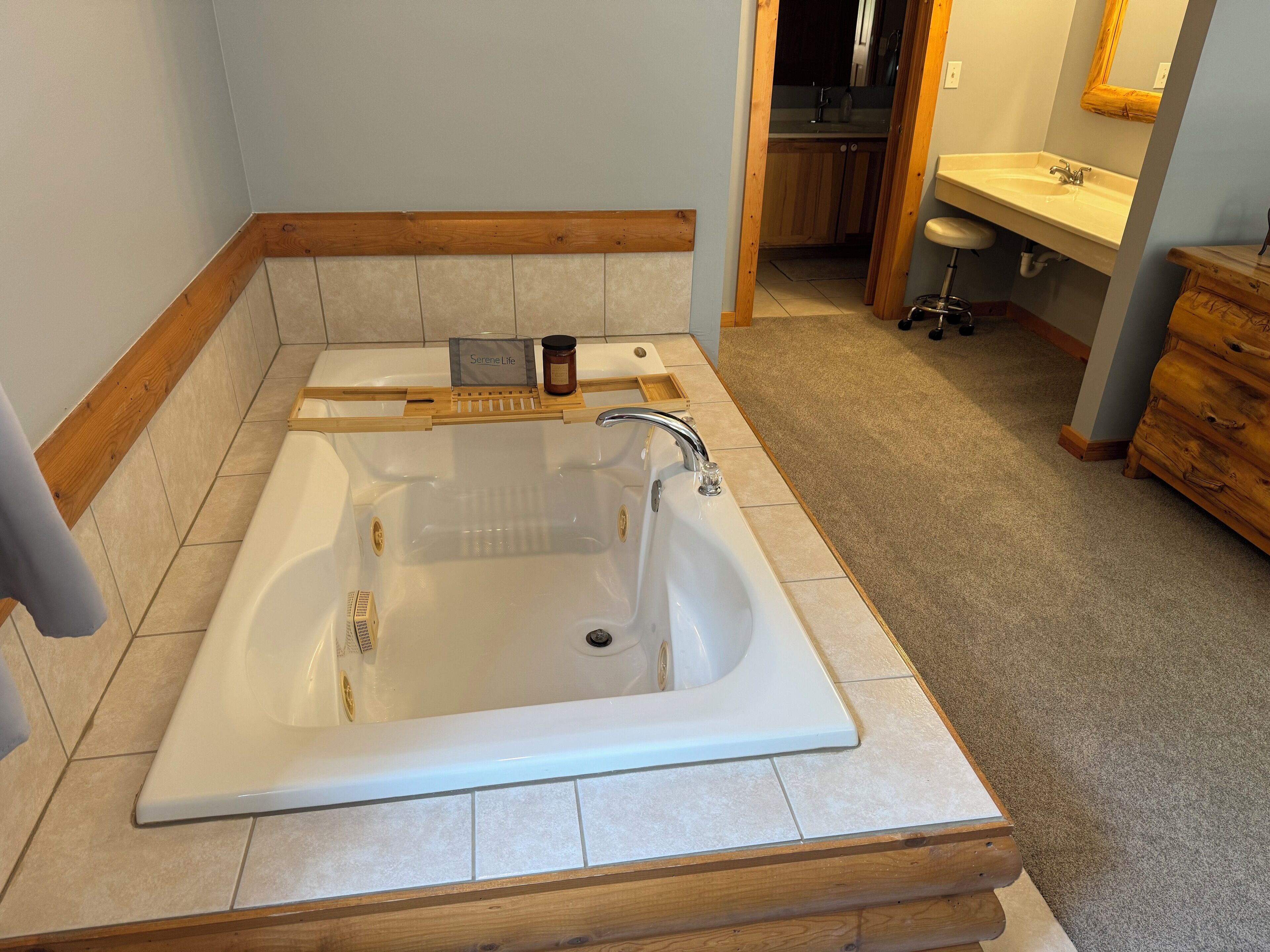 Un baño con una bañera grande, tocador de madera y lavamanos.