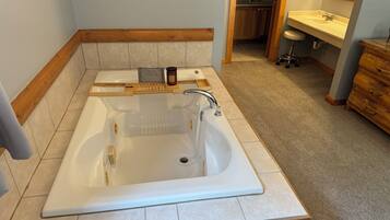 Un baño con una bañera grande, tocador de madera y lavamanos.