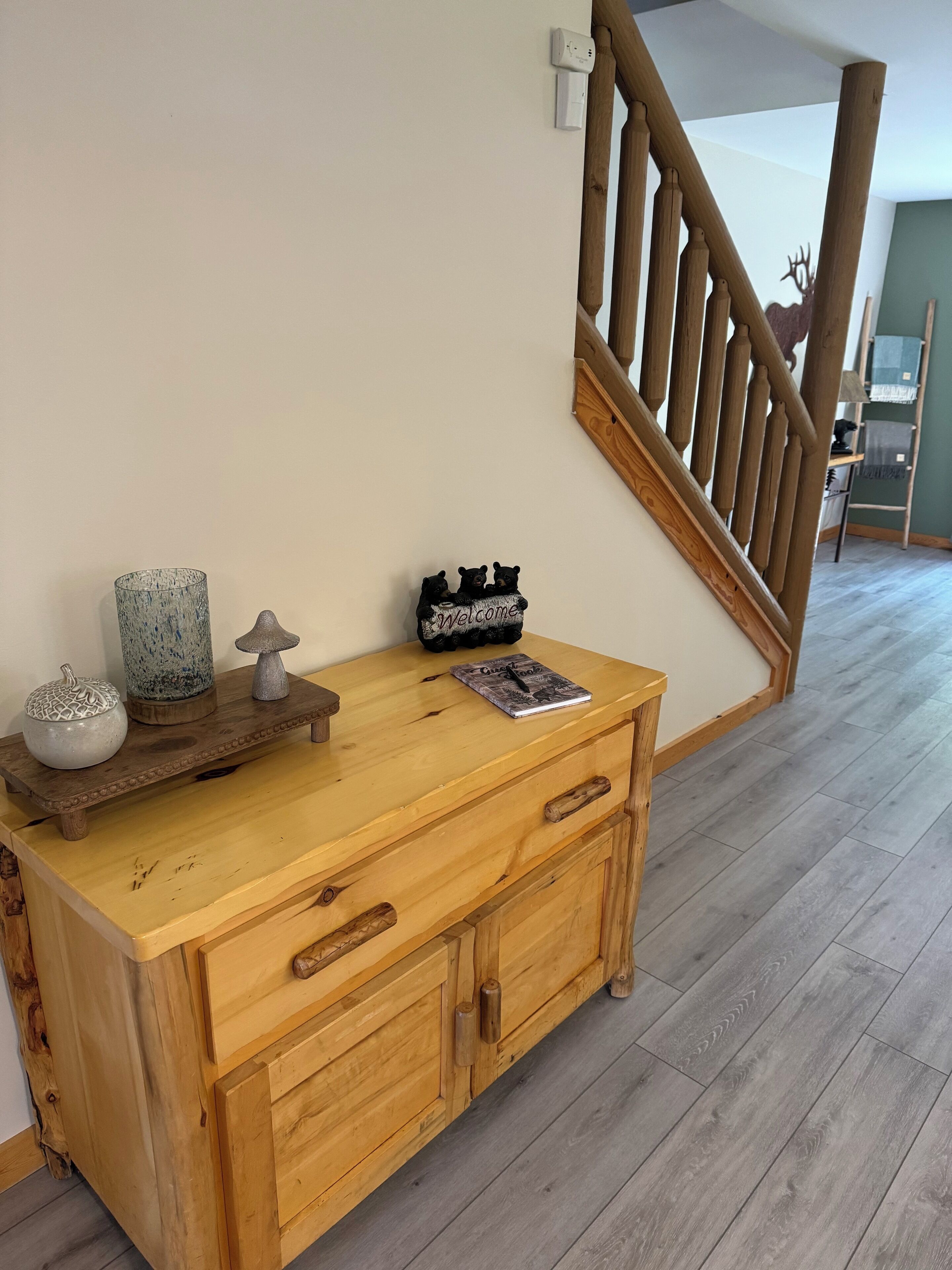 A wooden console table with drawers and a small shelf, a decorative bear sculpture, a welcome sign, and a lamp.