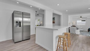 A modern kitchen with a stainless steel refrigerator, a white countertop, and wooden stools. - Holiday Lane - Discover the ultimate vacation retreat at Holiday Lane! (Naples)