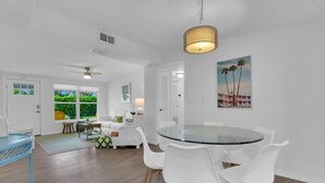 A modern living room with a glass-top dining table surrounded by white chairs, a ceiling fan, and a hanging light fixture. - Holiday Lane - Discover the ultimate vacation retreat at Holiday Lane! (Naples)